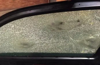 Close-up of a vehicle side window with a frosted web of cracks around several bullet impacts