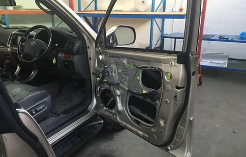 Front door of a Toyota opened in a workshop with the inner trim removed, showing the bare door shell